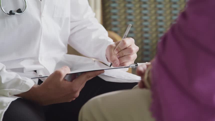 A doctor writes on a chart as he talks with a patient