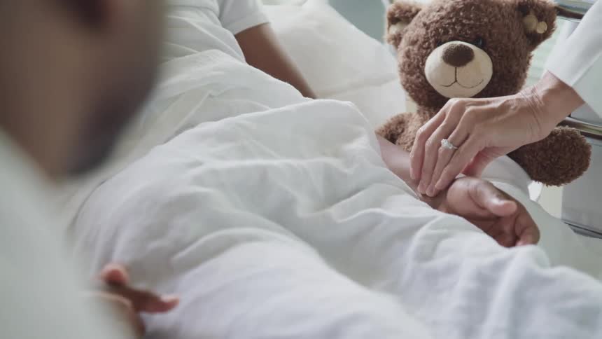 A teddy bear is in the hospital bed next to a patient