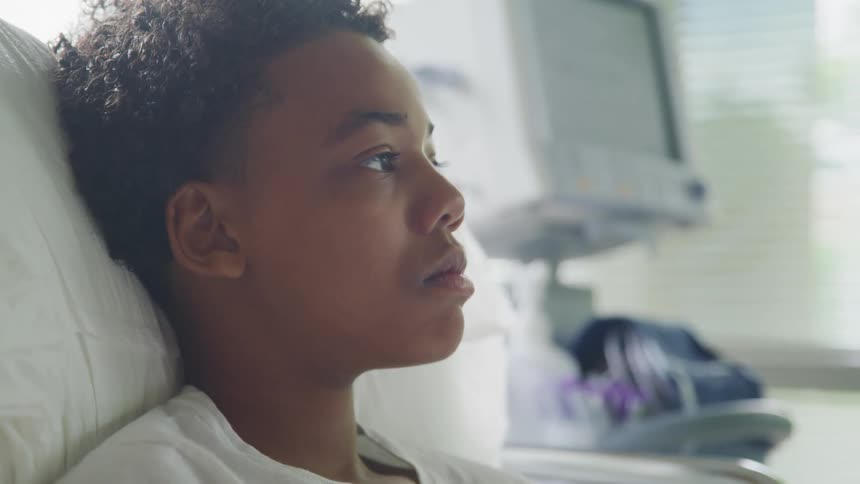 A boy rests in a hospital bed while lost in thought