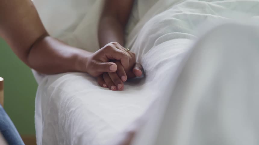 A woman holds her sons hand as he lies in a hospital bed