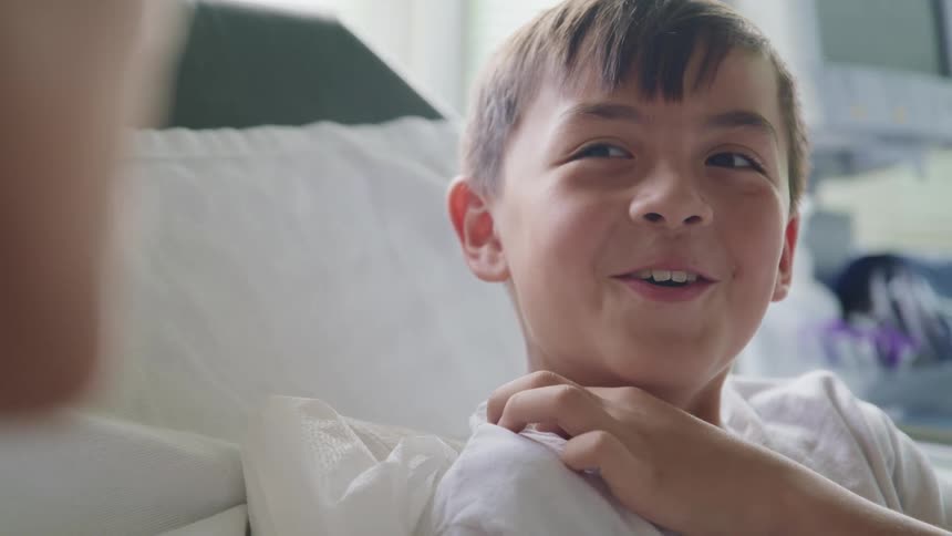 A young boy in a hospital bed smiles as he talks with someone