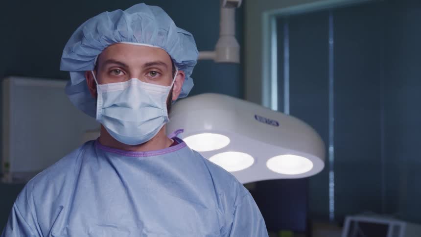 Man wearing surgical protective gear stands near lights and window