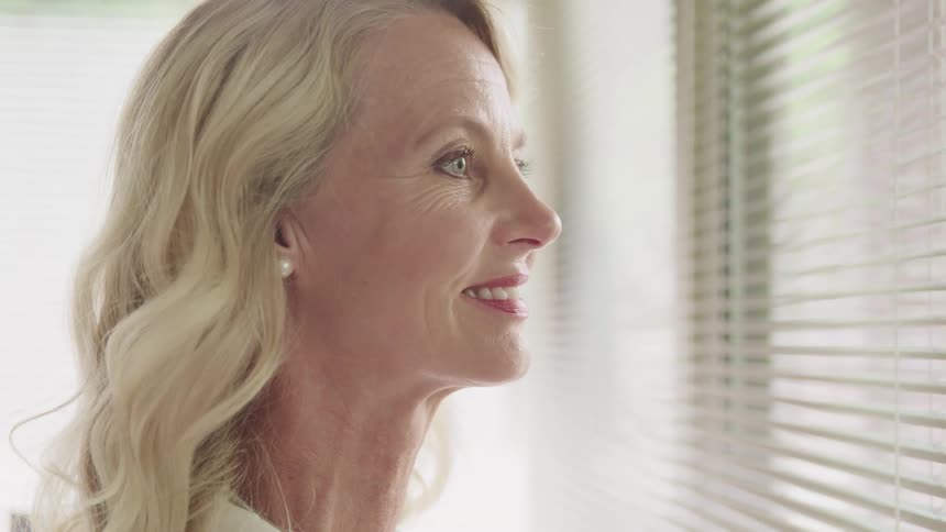 Blonde adult woman looks out a window while smiling