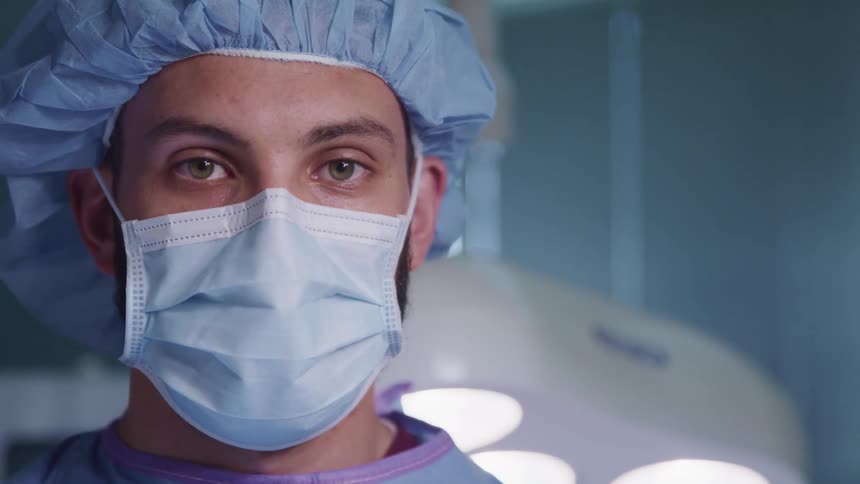 Surgeon wearing face mask and protective gear looks at the camera