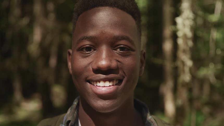 Young black man smiles broadly and faces the camera with eye contact in the forest
