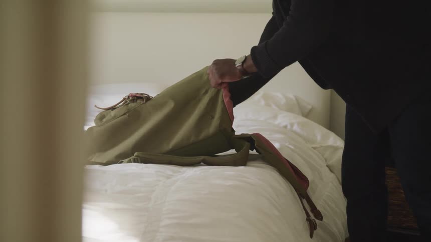 A person places a camera into a duffle bag that is sitting on a bed