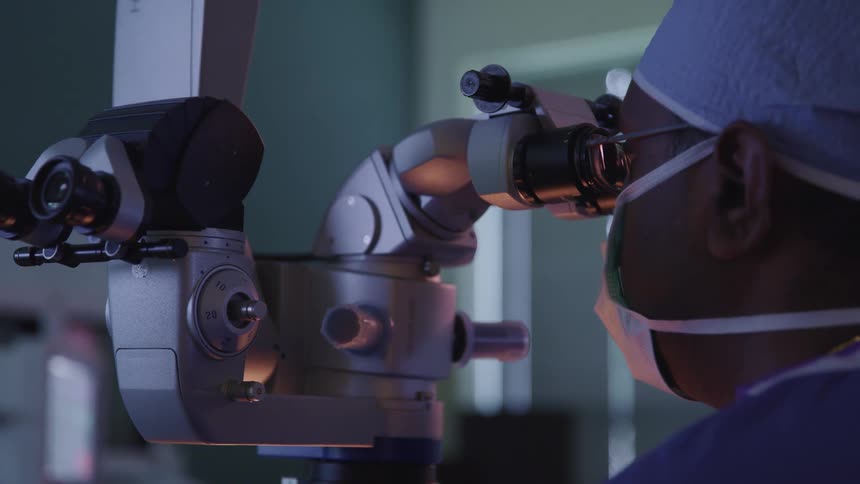 A surgeon looks through a microscope