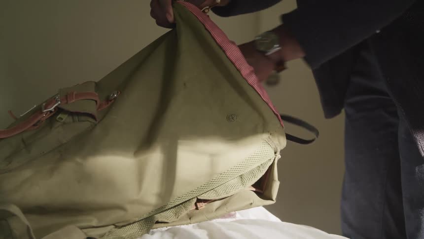 Black man picks up a camera and places it into a backpack