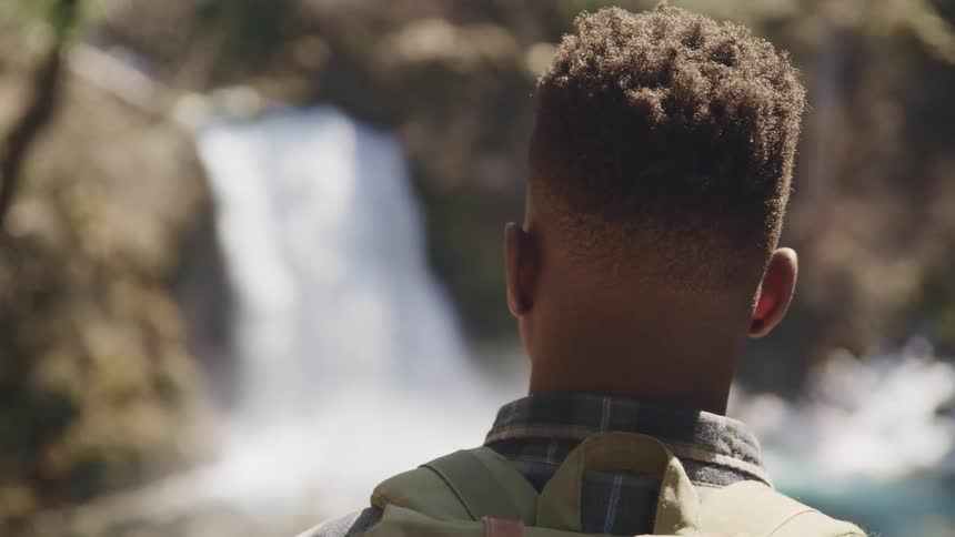 A man with a backpack standing looking at a waterfall and a cliff