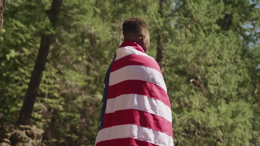 A teenage boy standing outside with an american flag draped over his shoulders