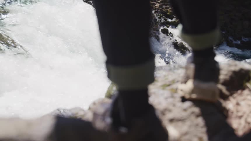 Man wearing jeans and sneakers stands on a rock and watches a waterfall