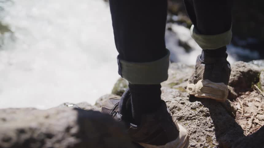 A person stands on a cliff and watches a water fall rushing down
