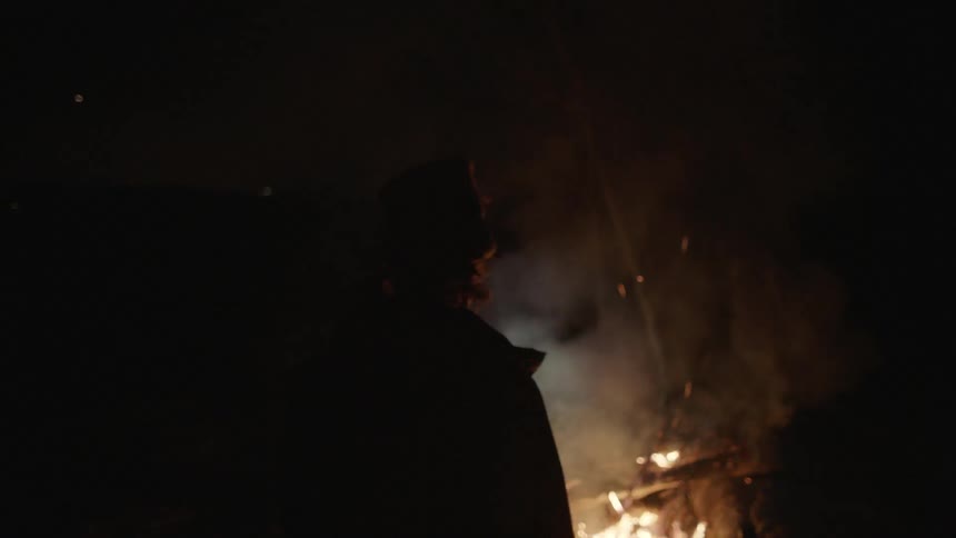 A person watches a burning campfire at night