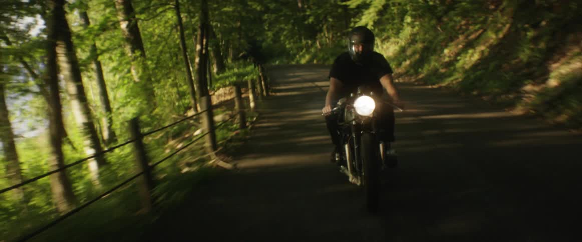 A man rides a motorcycle on a road by a hill
