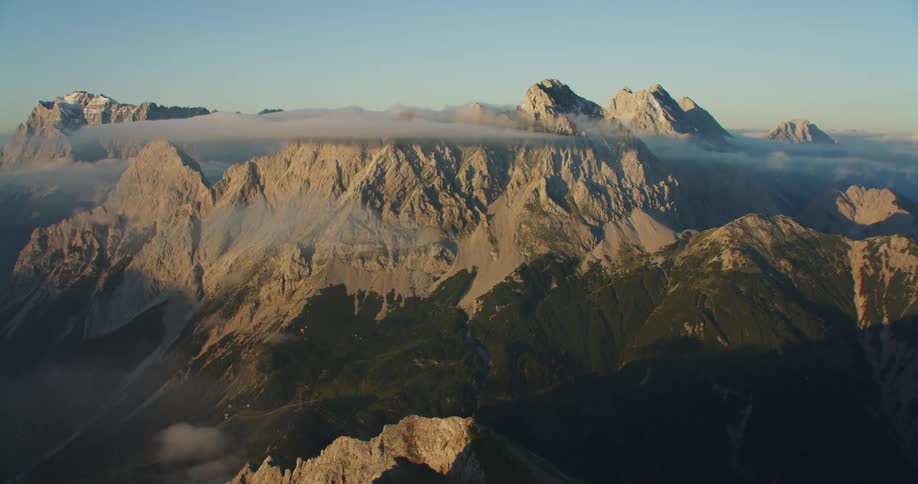 Aerial view of mountain range peaks over the clouds at sunset