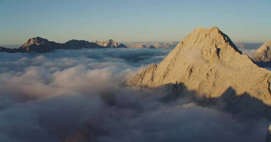 An aerial view of mountain peaks poking through clouds at dawn