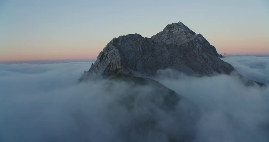 An aerial view of a mountain covered by clouds is displayed