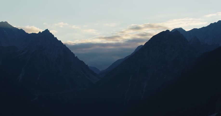 A ridge of barren stone mountains under a clear sky as dark clouds loom in the distance
