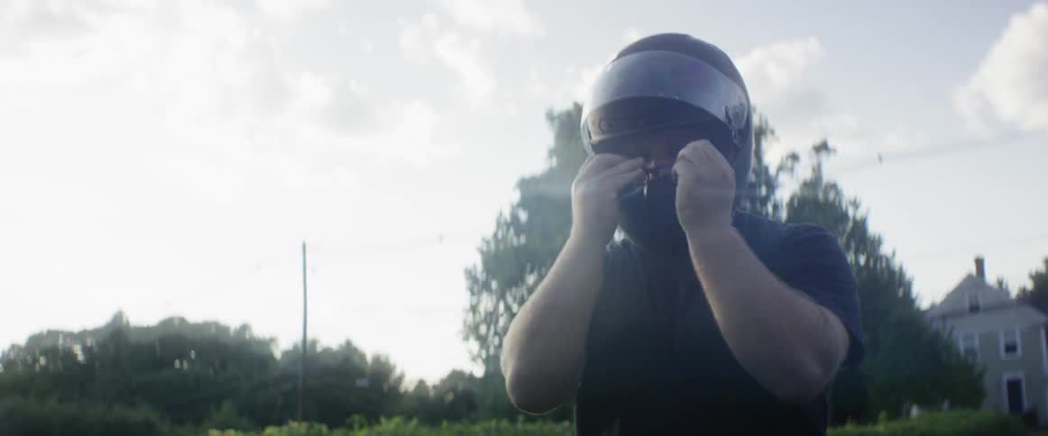 A bearded man puts on his helmet and gets on his bike