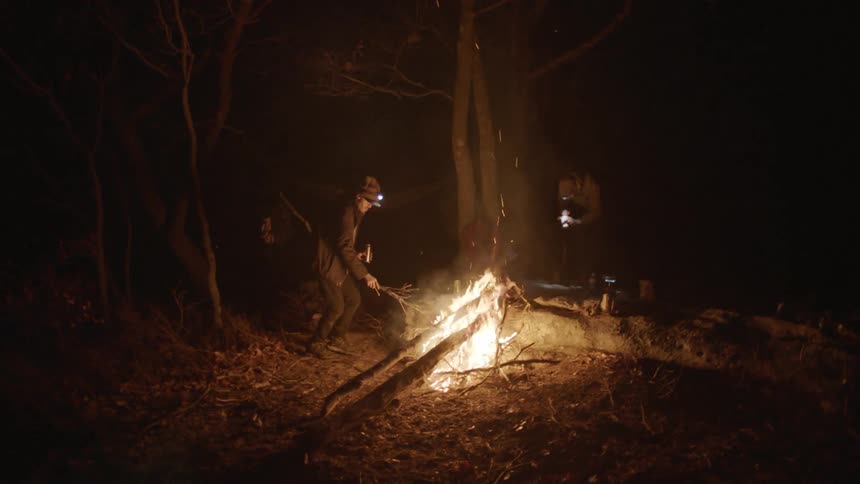A man adding sticks to a campfire