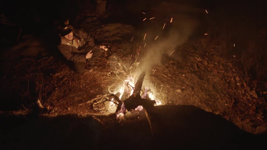 A man adds a stick to a campfire