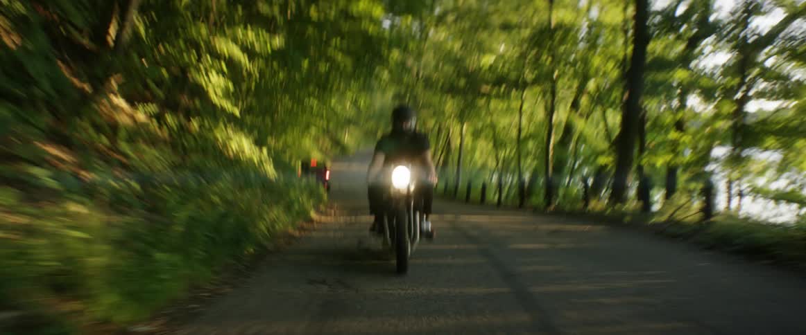 A motorcyclist rides on a road in a wooded area