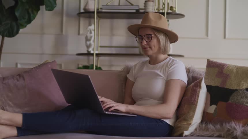 A woman is sitting on a couch and looking at a laptop