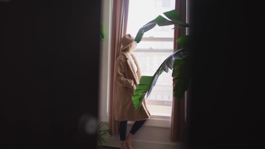 A woman stands by her window looking outside