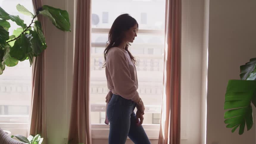 A woman stands by the window in her home
