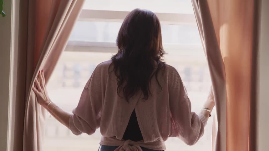 A woman is opening the window curtains