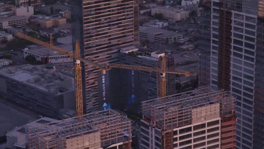 A construction crane looming over the scaffolding of a skyscraper in a metropolis in the evening