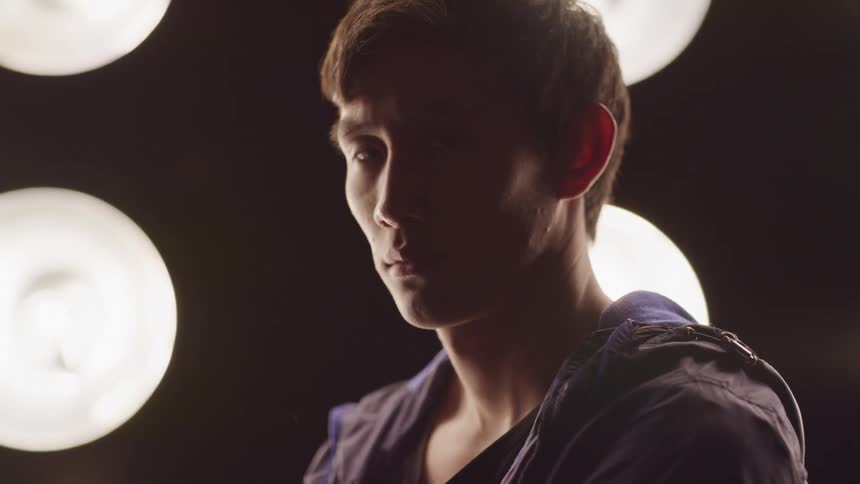An asian male standing near spotlights looking sad