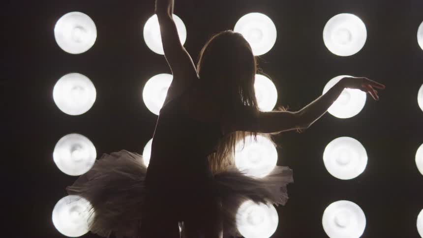 A ballerina in a tutu dances in front of a large stage light array