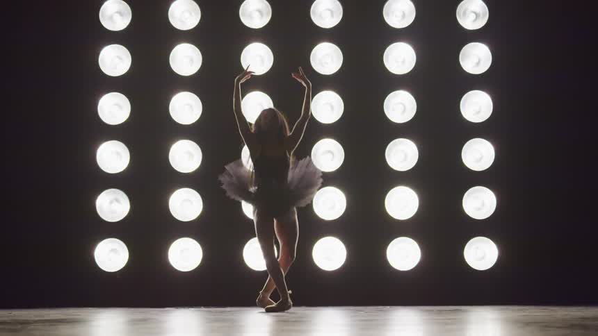 A ballerina wearing a tutu performs various ballet dance moves in front of a wall covered in lights