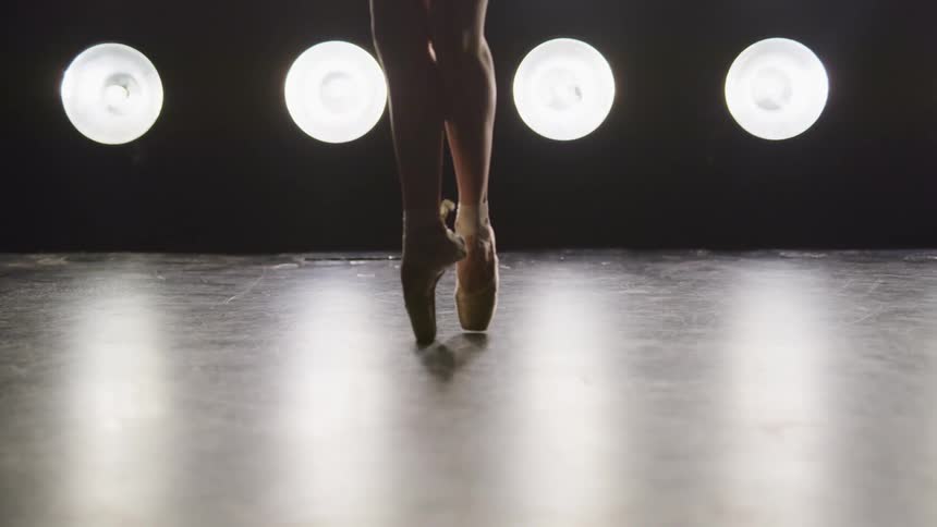 A ballerina dances en pointe on a stage with spotlights