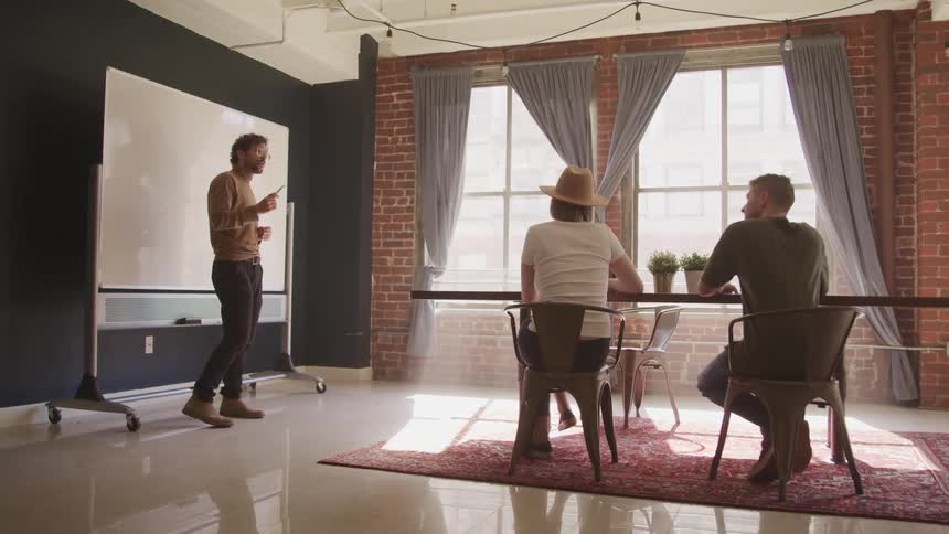 Man in front of a whiteboard talks to coworkers in a meeting at the studio office