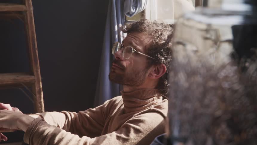 A man sitting on the floor in his home looks like he is about to cry