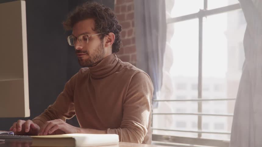 Man sits at desk near window showing city typing on computer
