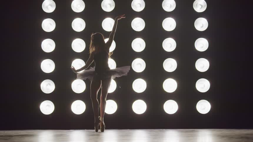 Silhouette of a woman wearing ballet shoes and a tutu performing classical ballet on stage