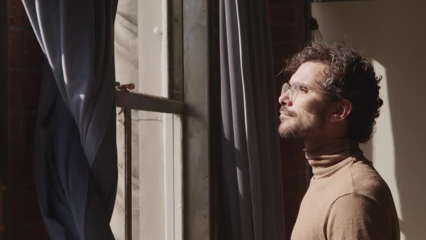 A man is looking out a window while standing indoors