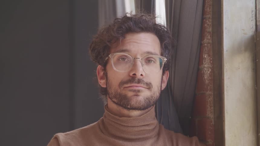 A man is standing inside his house while wearing glasses