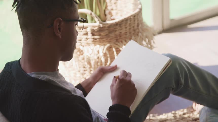 A man with glasses drawing with a pencil on a notepad