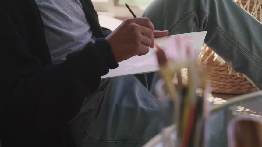 A man sitting inside paints on a canvas