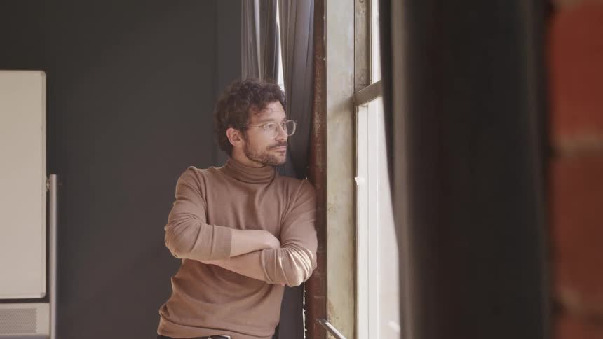 A man is standing in a room and looking out the window