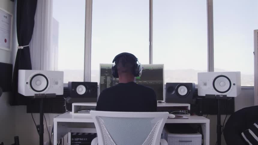 A man in his office works on his computer that is surrounded by speakers
