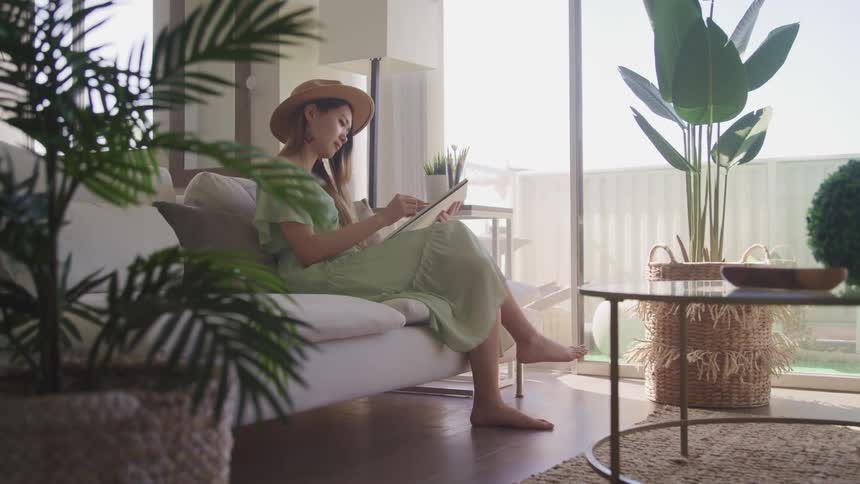 A woman sits on a couch with a notepad and writing instrument