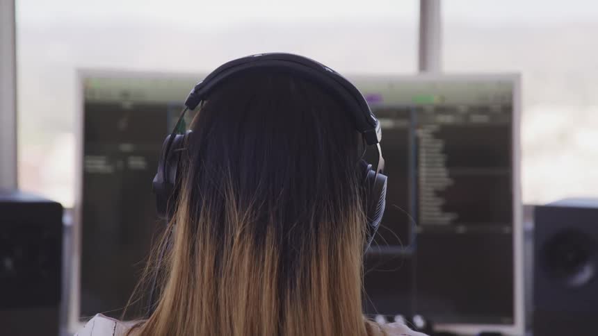 A woman with headphones on sits at a desk and works on a computer