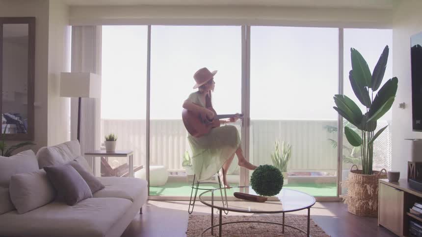 A woman sits in her house and plays the guitar