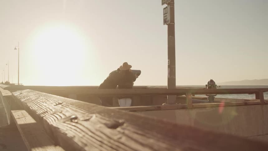 Elderly couple shares binoculars on the pier next to the ocean at sunset