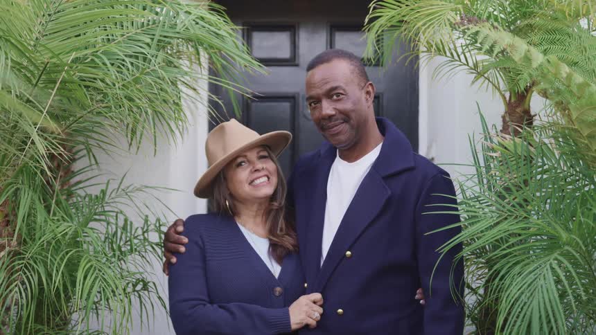 Couple wearing similar colored clothing stand before front door smiling
